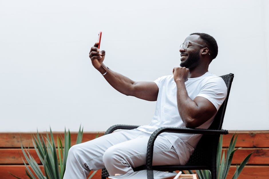 A happy man in a white shirt sits outdoors using his smartphone for a video call.