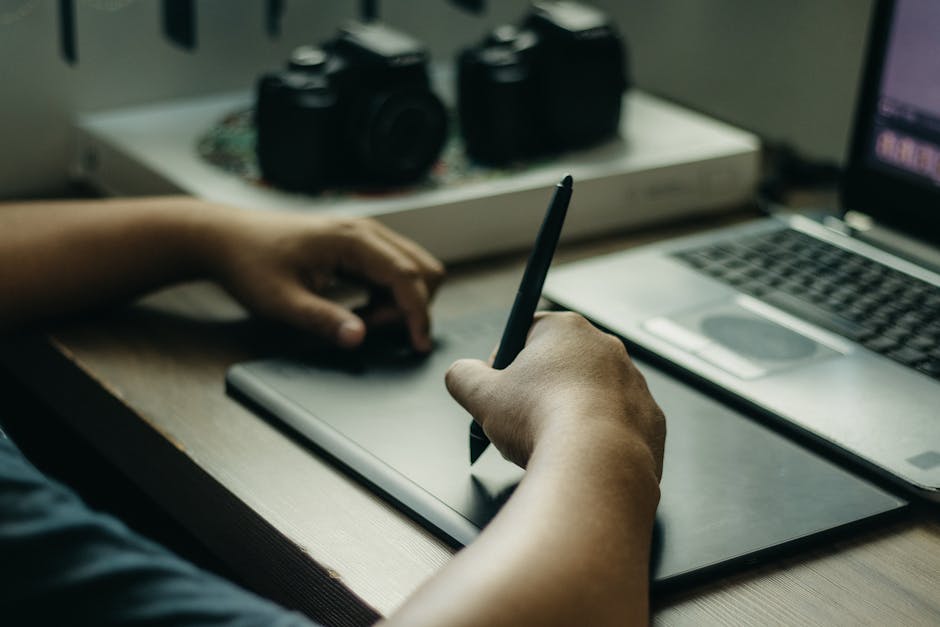Person using a graphic tablet alongside laptop for digital design work indoors.