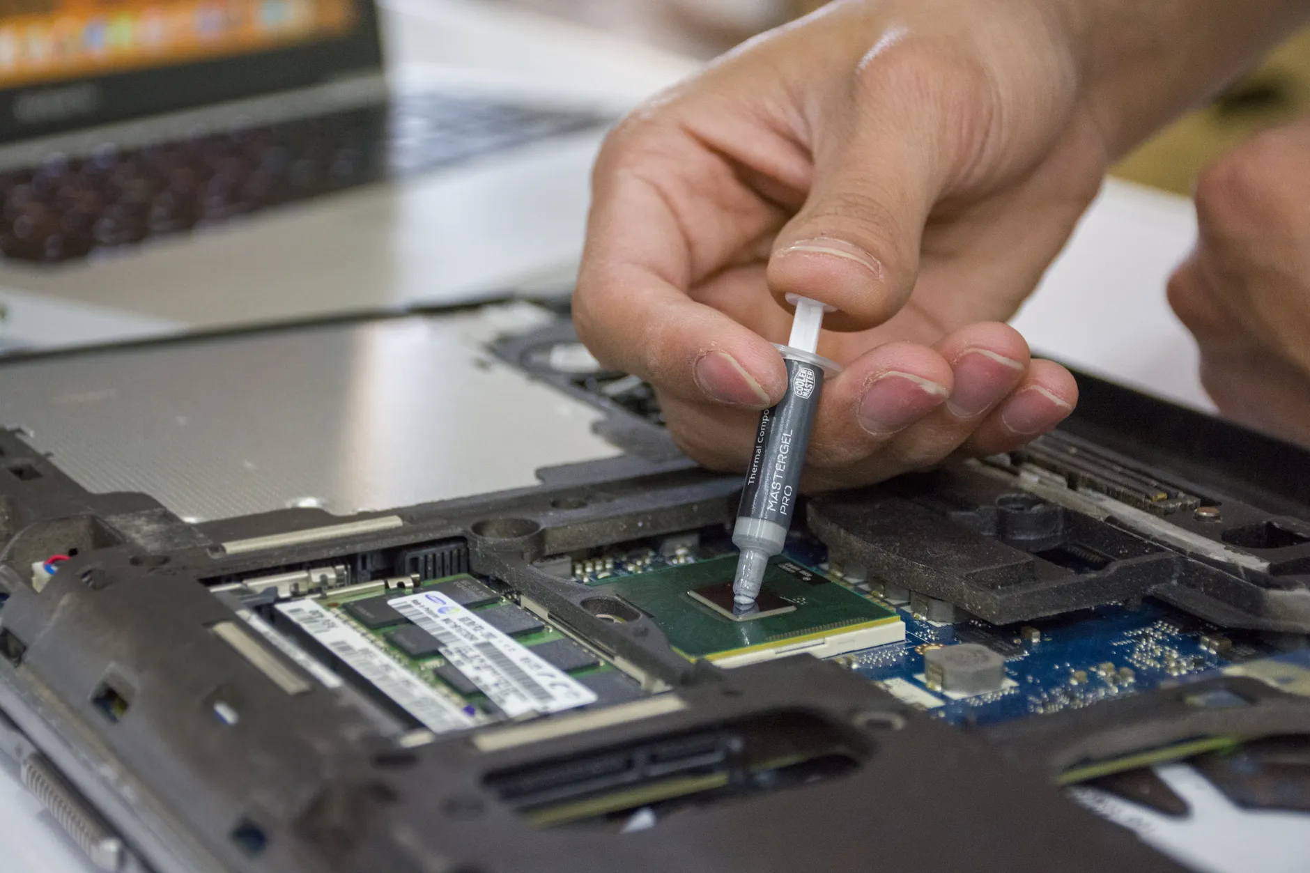 Hero image of Clean close-up of the Thermal Grizzly Kryonaut syringe held over an open laptop CPU, showing the exact product in a real repasting context