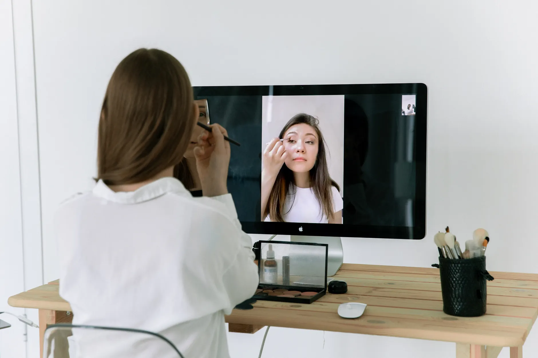 Hero image of Clean, well-lit photo of a person sitting at a desk in front of a laptop or monitor with a webcam mounted on top, showing a clear, bright video call setup in a home office environment