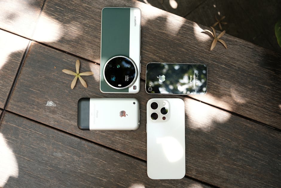 Assorted smartphones displayed outdoors on a wooden table under dappled sunlight.