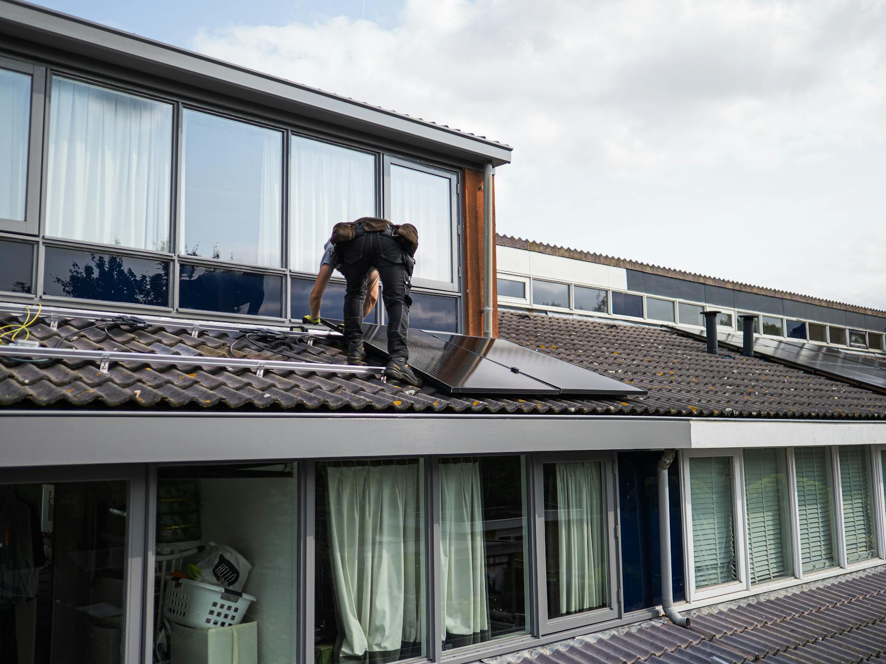 Installation image of Solar installer in safety gear hands on mounting solar panels on a home roof, real-world in use photo